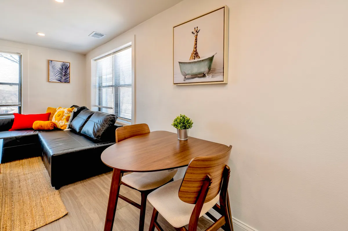 A cozy living and dining area featuring playful giraffe artwork, a comfortable sofa, and a central dining table. Natural light brightens the space, highlighting eclectic decor that reflects an artistic, vibrant lifestyle.