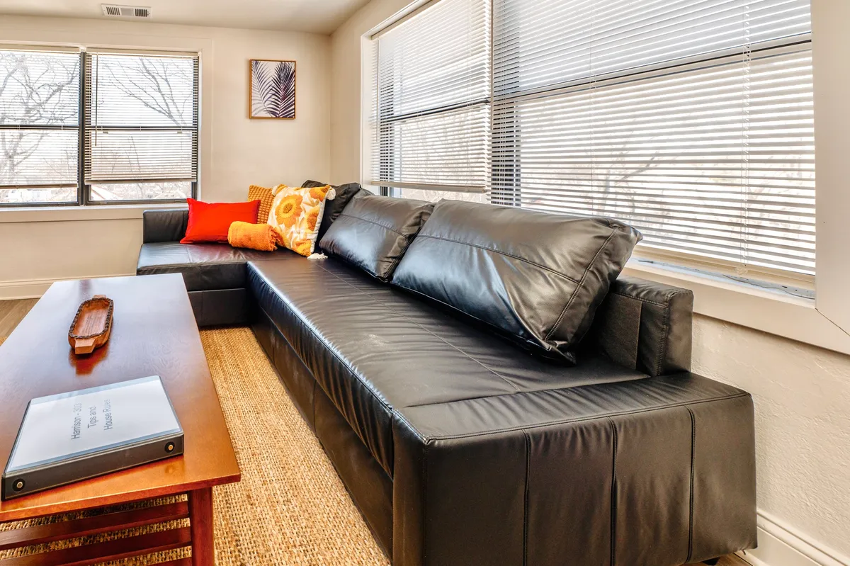 A modern living space highlighted by a black leather sectional sofa, colorful throw pillows, and a wooden coffee table. The space feels warm, welcoming, and perfect for both reading and entertaining guests.