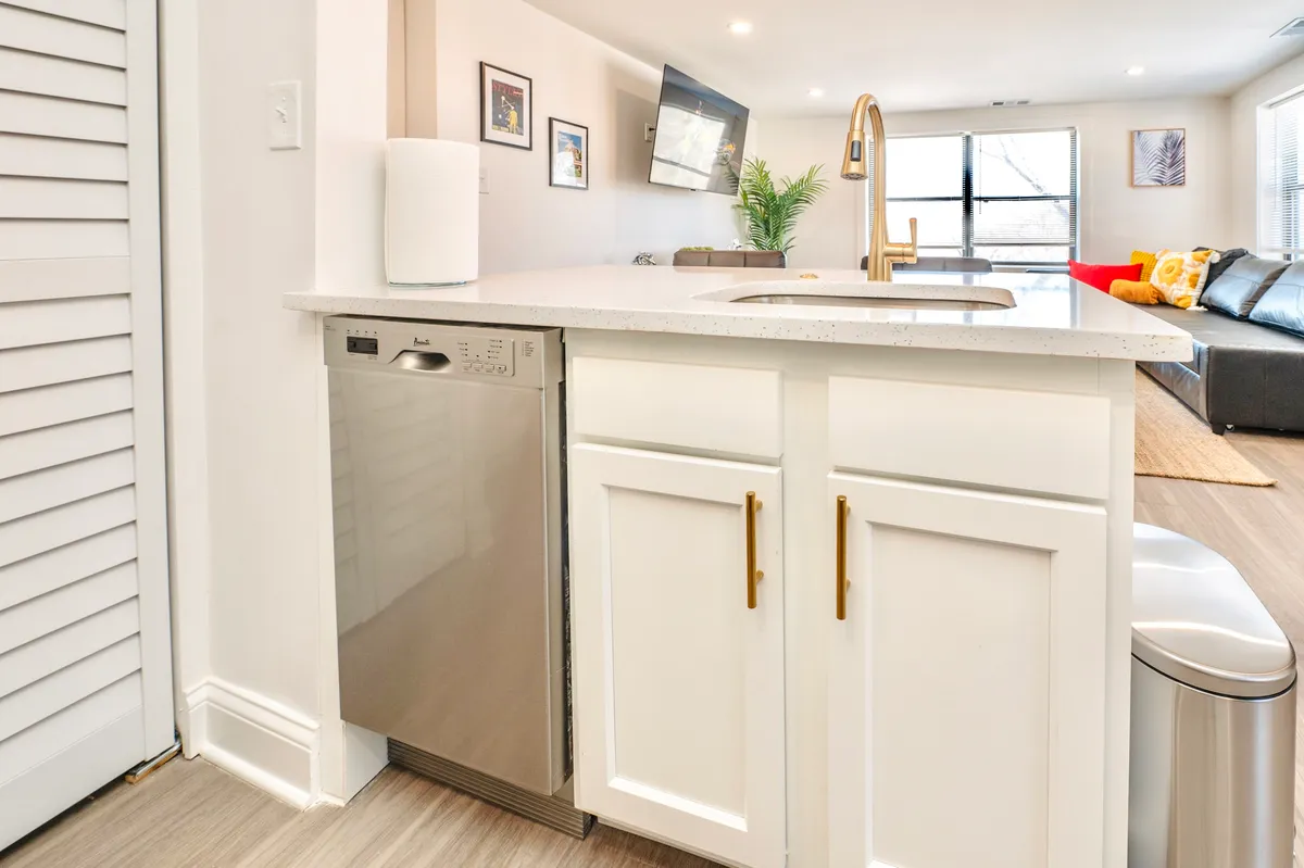A modern kitchen space showcasing a stainless steel dishwasher, a striking golden faucet, and a spacious kitchen counter. The area exudes a welcoming atmosphere, suitable for cooking, entertaining, or simply relaxing after a long day.